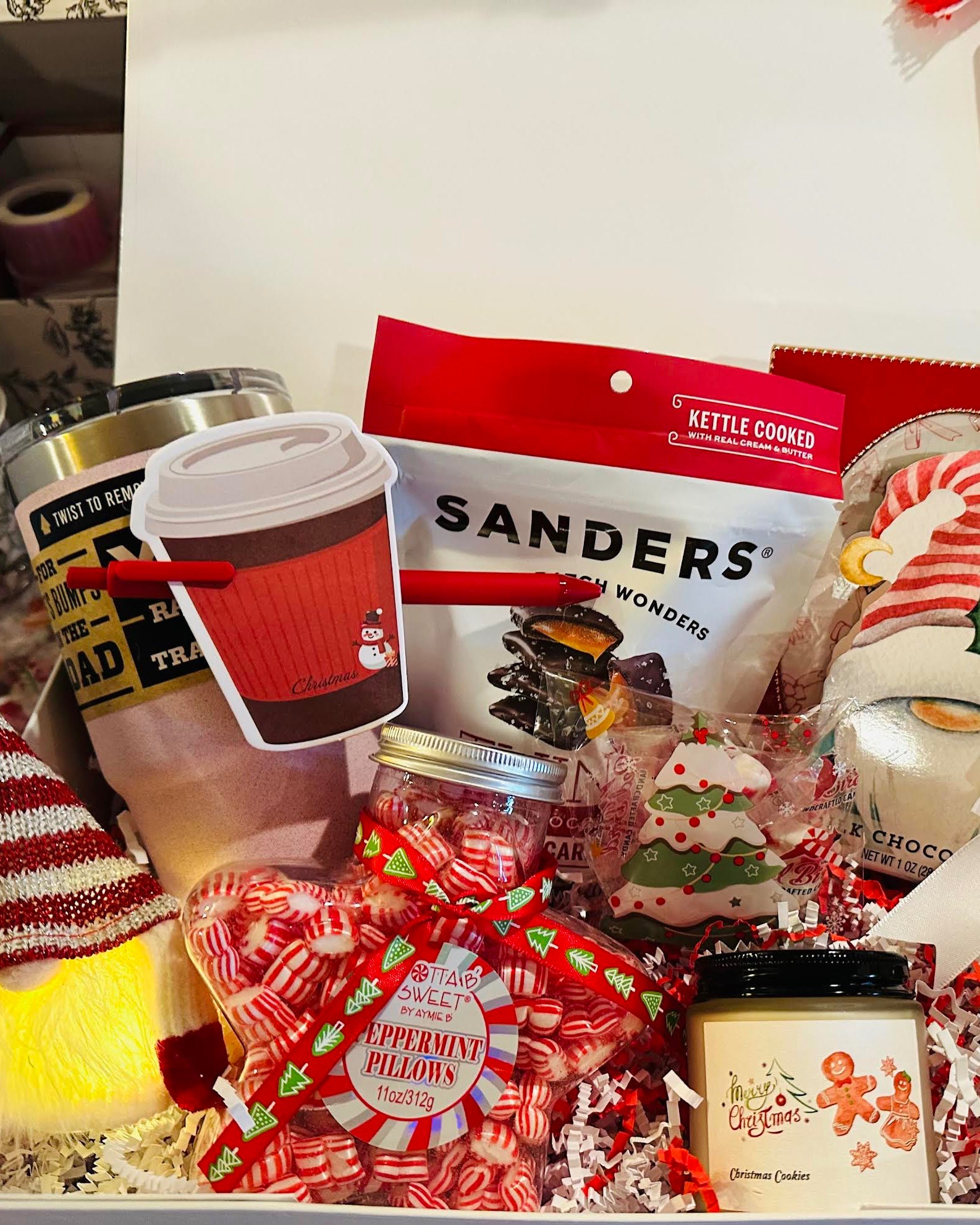 Holiday-themed gift box with candy, coffee, and decorative items on a table.