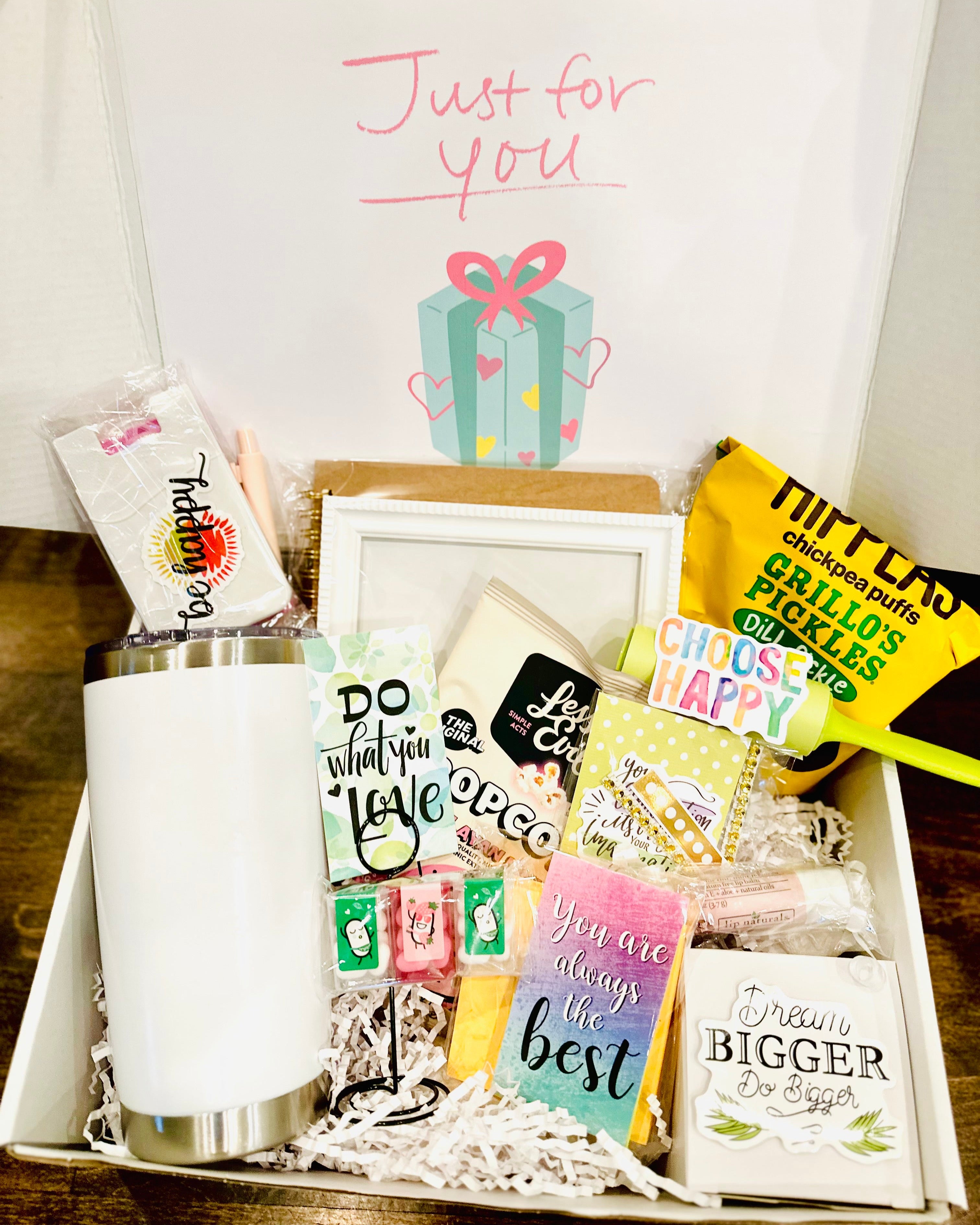 Gift basket with various items including a mug, cards, and a box on a wooden surface.