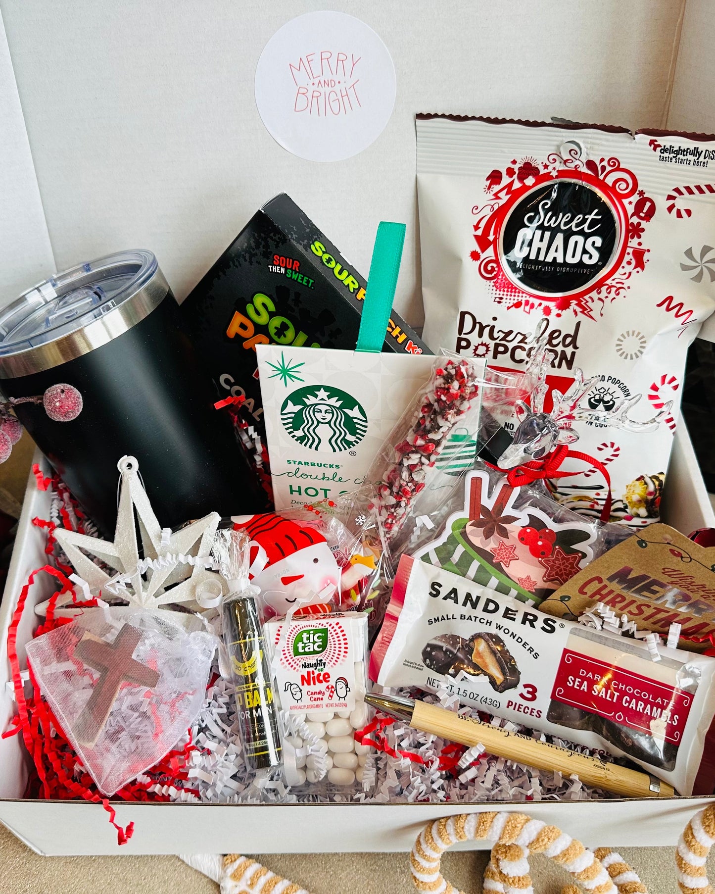 Gift box with various items including snacks, a Starbucks coffee cup, and decorative elements on a checkered surface.
