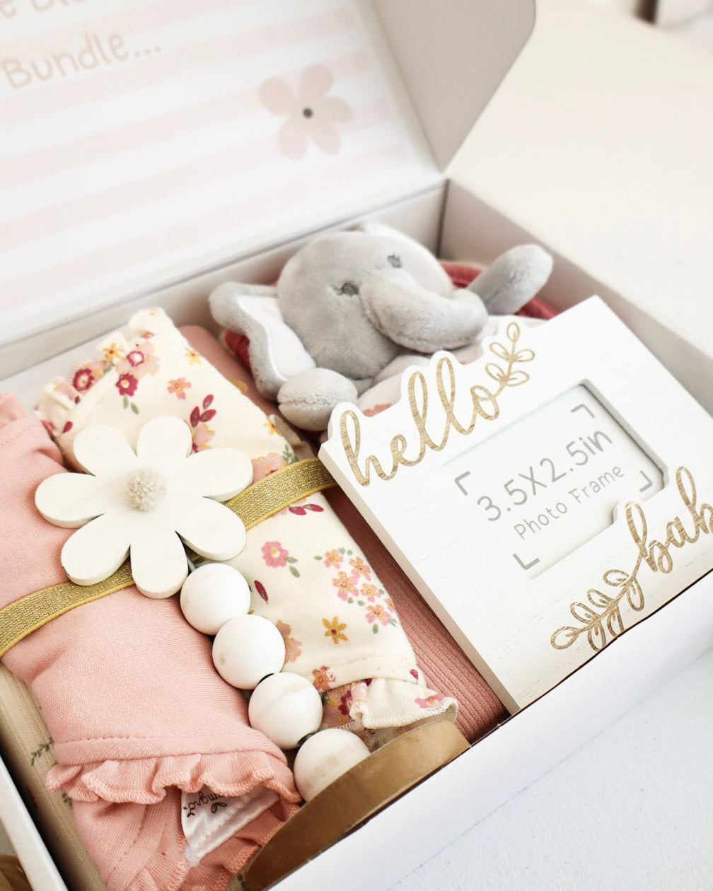 Baby gift set with pink outfit, floral blanket, gray elephant toy, and 'hello baby' card in a box.
