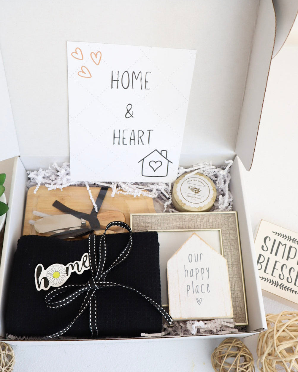 Gift box with decorative items including a black bag with 'home' text, a small clock, and cards.